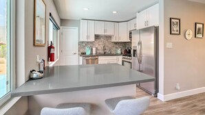 Une cuisine moderne avec des meubles blancs, un îlot central et un réfrigérateur en acier inoxydable.