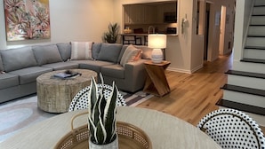 A modern living room with a grey sectional sofa, a round coffee table, and a dining area with a white table and chairs. - Convenient to Beach, restaurants, shopping and much more! (Wilmington)
