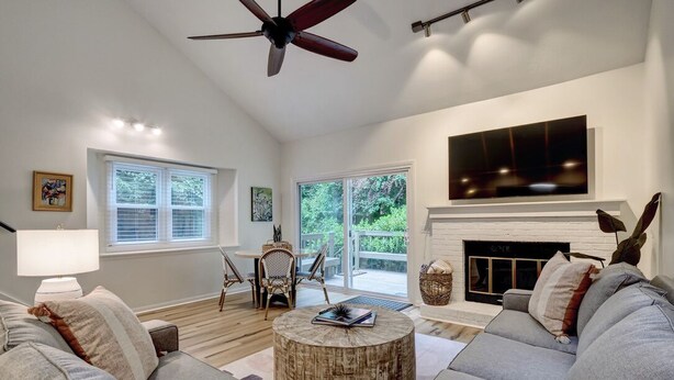 A living room with a fireplace, a ceiling fan, and a large window overlooking greenery. - Convenient to Beach, restaurants, shopping and much more! (Wilmington)