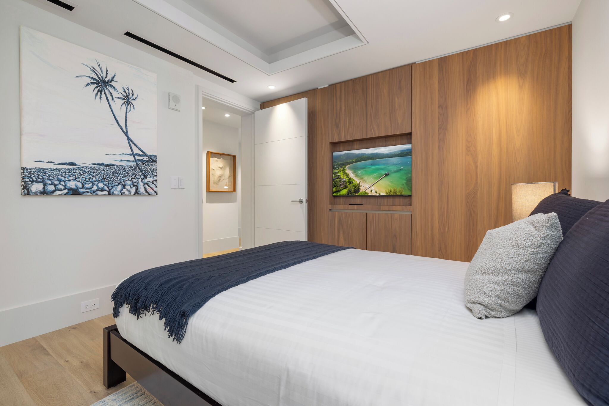 Ein modernes Schlafzimmer mit einem großen Bett, Holzvertäfelung, einem Fernseher und Kunstwerken an den Wänden.