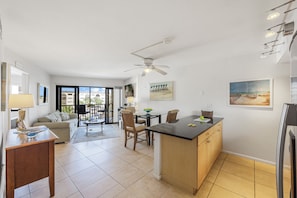 A modern kitchen with a central island, a dining area with chairs and a table, and a living room with a sofa and a coffee table.