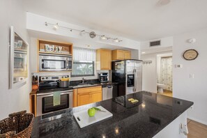 A modern kitchen with stainless steel appliances, wooden cabinets, and a black granite countertop.