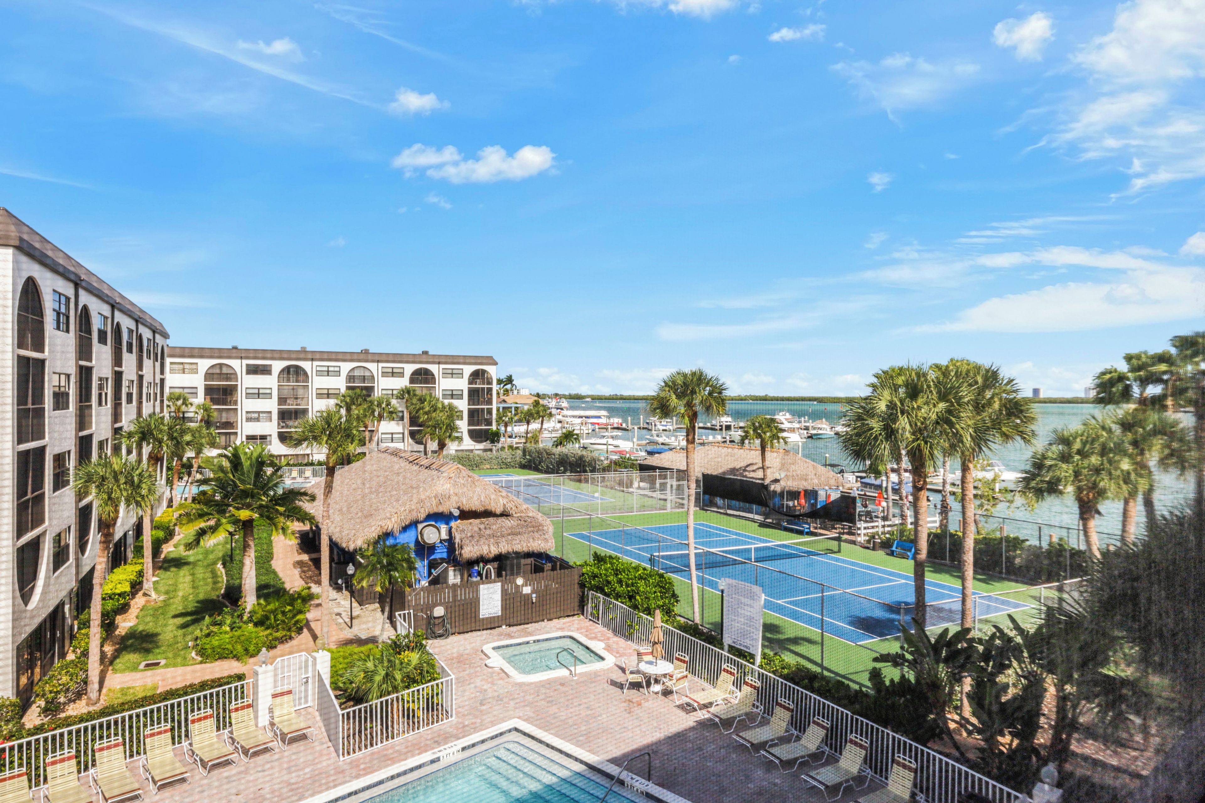 A resort with a pool, tennis courts, and a view of the sea.