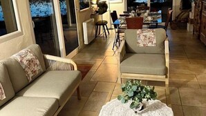 A spacious living area with a sofa, chairs, a dining table, and a view through large windows.
