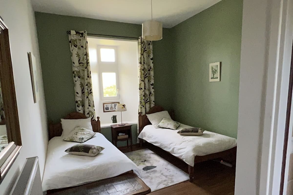 Een kamer met twee bedden, een tafeltje, een stoel en een radiator.