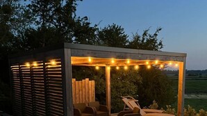 A wooden deck with outdoor furniture, string lights, and a pergola structure.