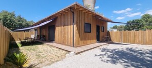 A wooden cabin with a covered patio, a door, and a window. - Maison Neuve Bardage Bois Bassin d Arcachon (Lanton)