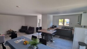 Ein modernes Wohnzimmer mit Sofa, einem Esstisch mit Obstschale und einer Küchenzeile mit Barhocker.