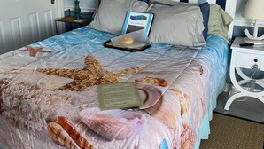 Cama arrumada com estrela-do-mar e um bilhete de agradecimento, cabeceira listrada e mesa de cabeceira pequena com luminária.
