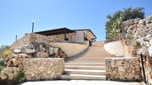 Un escalier en pierre menant à un bâtiment doté d’un toit plat et d’une pergola.