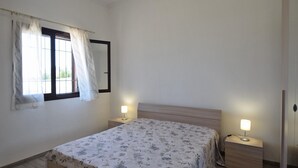 Une chambre à coucher comprenant un lit, deux tables de chevet, une commode, une fenêtre avec des rideaux et un miroir.