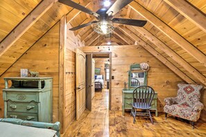 Une chambre mansardée en bois, avec un plafond en pente, un ventilateur de plafond, une commode, une chaise et un lit.