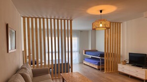 A modern room with a sofa, a wooden table, a bunk bed, a television, and a decorative light fixture. - 'Loft Palamós' Apartment with A/C (Palamos)