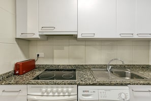 Cozinha com armários brancos, torradeira vermelha, fogão, lava-louças e bancada de granito.