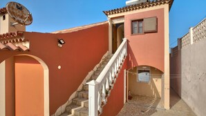 Ein Gebäude mit roter Fassade, einer weißen Treppe mit Balustraden, einer Satellitenschüssel und einem kleinen Fenster mit Fensterläden.