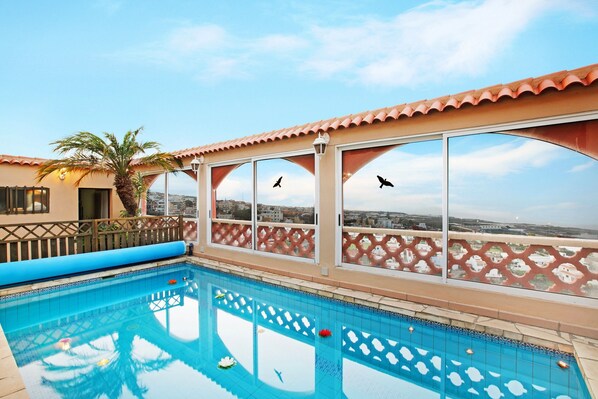Piscina en la azotea con vistas a la ciudad, una palmera y un deck con baldosas.
