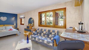 A bedroom with a bed, a sofa, a small table, a window, and a bedside lamp.
