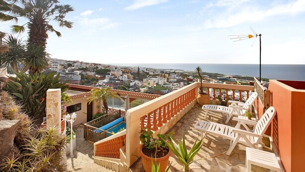 A terrace with lounge chairs, a pool, and a view of the sea and town.