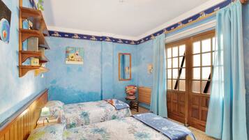 A bedroom with two beds, a wooden shelf, a chair, a window with curtains, and a door.