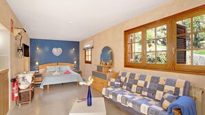 A bedroom with a bed, a sofa, a small table, a mirror, and a window.