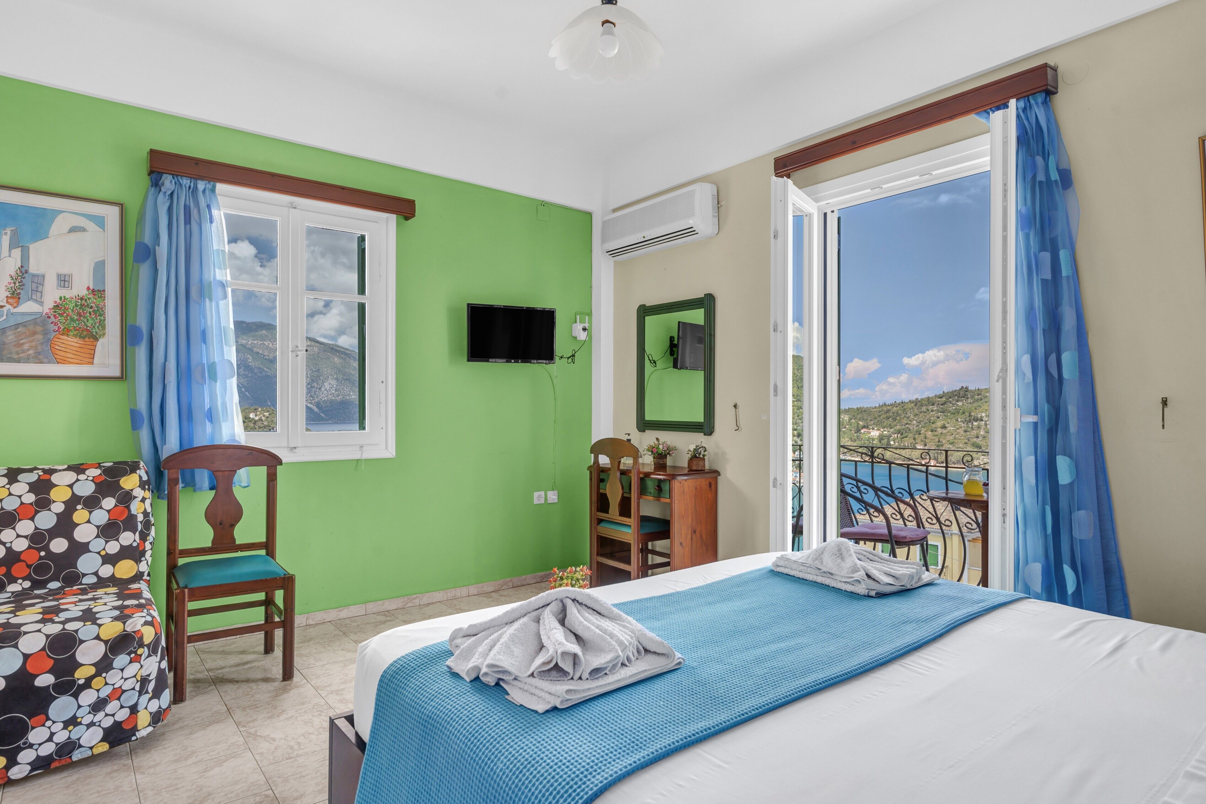 A hotel room with a bed, a chair, a desk, a TV, and a balcony with a view.
