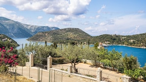 Paisatge costaner amb vista despejada al mar, muntanyes i una propietat tancada amb mur de pedra.