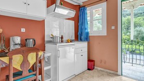 Une cuisine compacte avec des meubles blancs, une cuisinière encastrée et une fenêtre donnant sur un espace verdoyant.