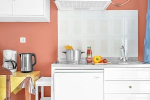 Una cocina con encimera blanca, cafetera, hervidor, olla, botella de salsa y un pimiento.