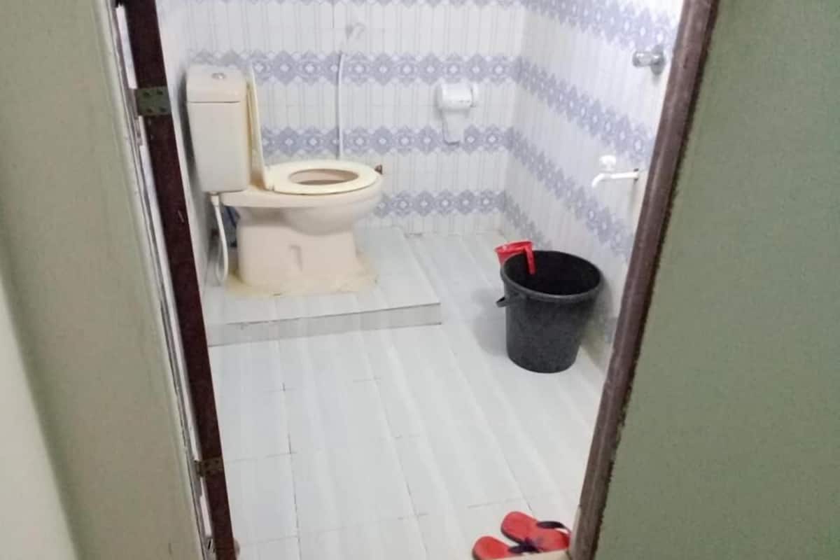 Een badkamer met een toilet, een emmer en een paar slippers.