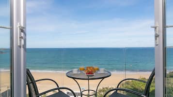 Een balkon met een tafel en twee stoelen met uitzicht op een strand.