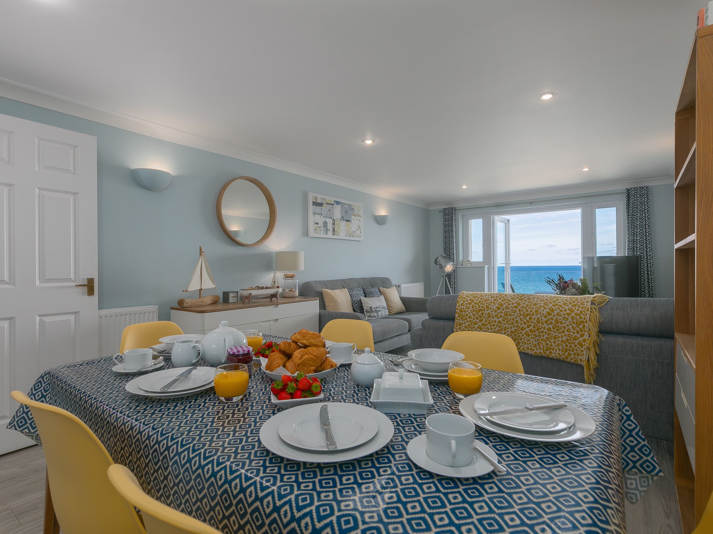 A dining area with a table set for breakfast, a sofa, and a view of the sea.
