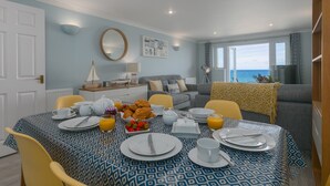 Un comedor con una mesa dispuesta para el desayuno, un sofá y vista al mar.