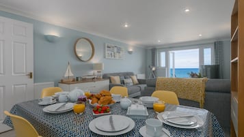 Een eetgedeelte met een ontbijt gedekte tafel, een bank en uitzicht op zee.