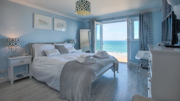 Un dormitorio con cama, mesitas de noche, lámpara, televisión y vistas al mar.