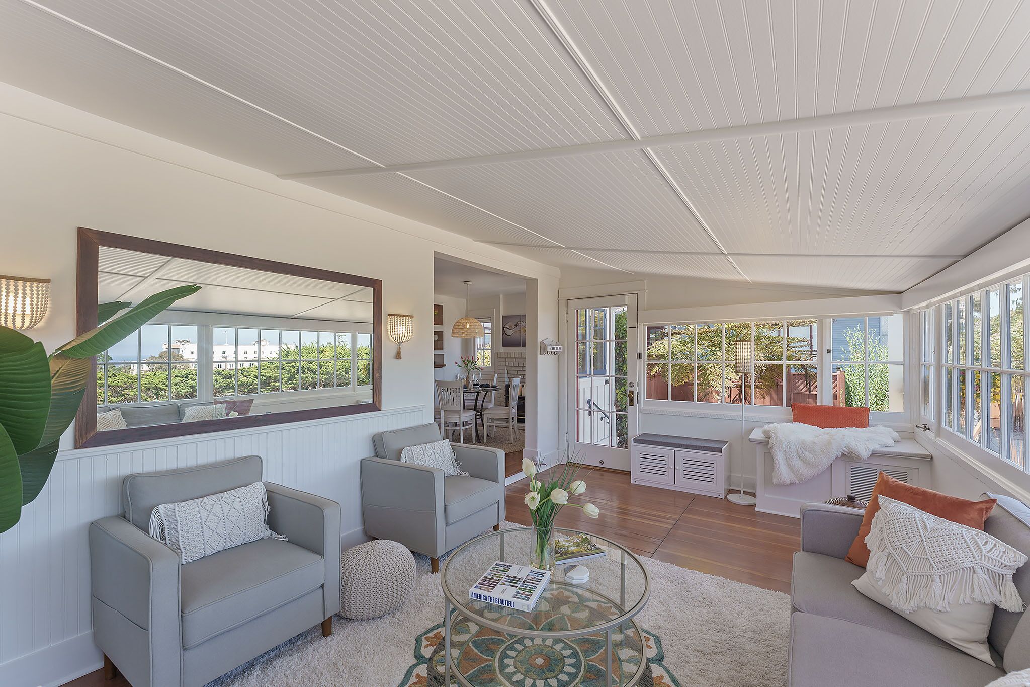 A spacious living room with a large window, a sofa, a coffee table, and a dining area visible through the window.
