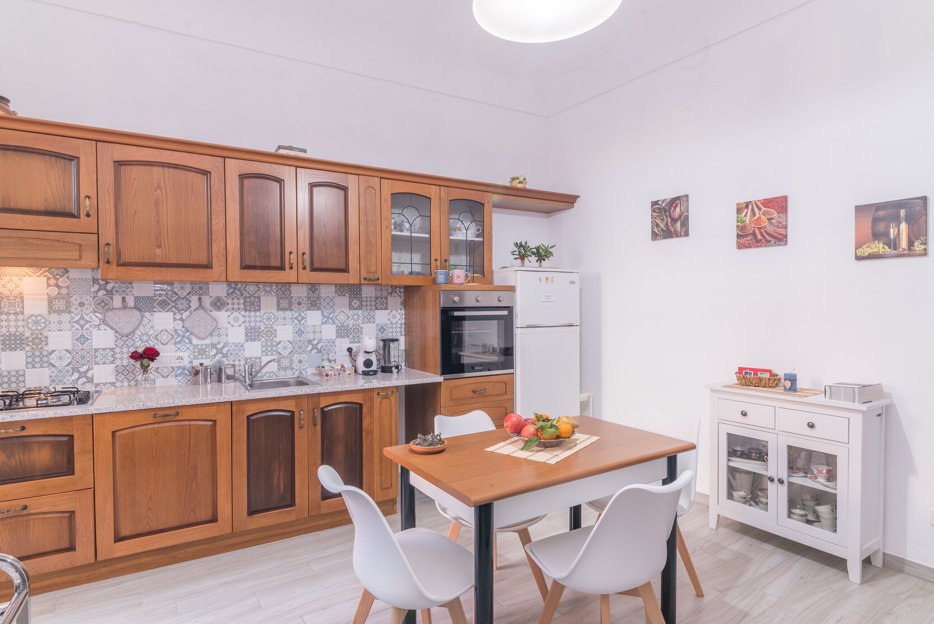 Une cuisine avec des meubles en bois, un réfrigérateur blanc, une table à manger avec des chaises et un meuble avec des portes en verre.