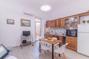 Una cocina compacta con armarios de madera, una mesa de comedor con sillas, un televisor sobre un carrito y un refrigerador.
