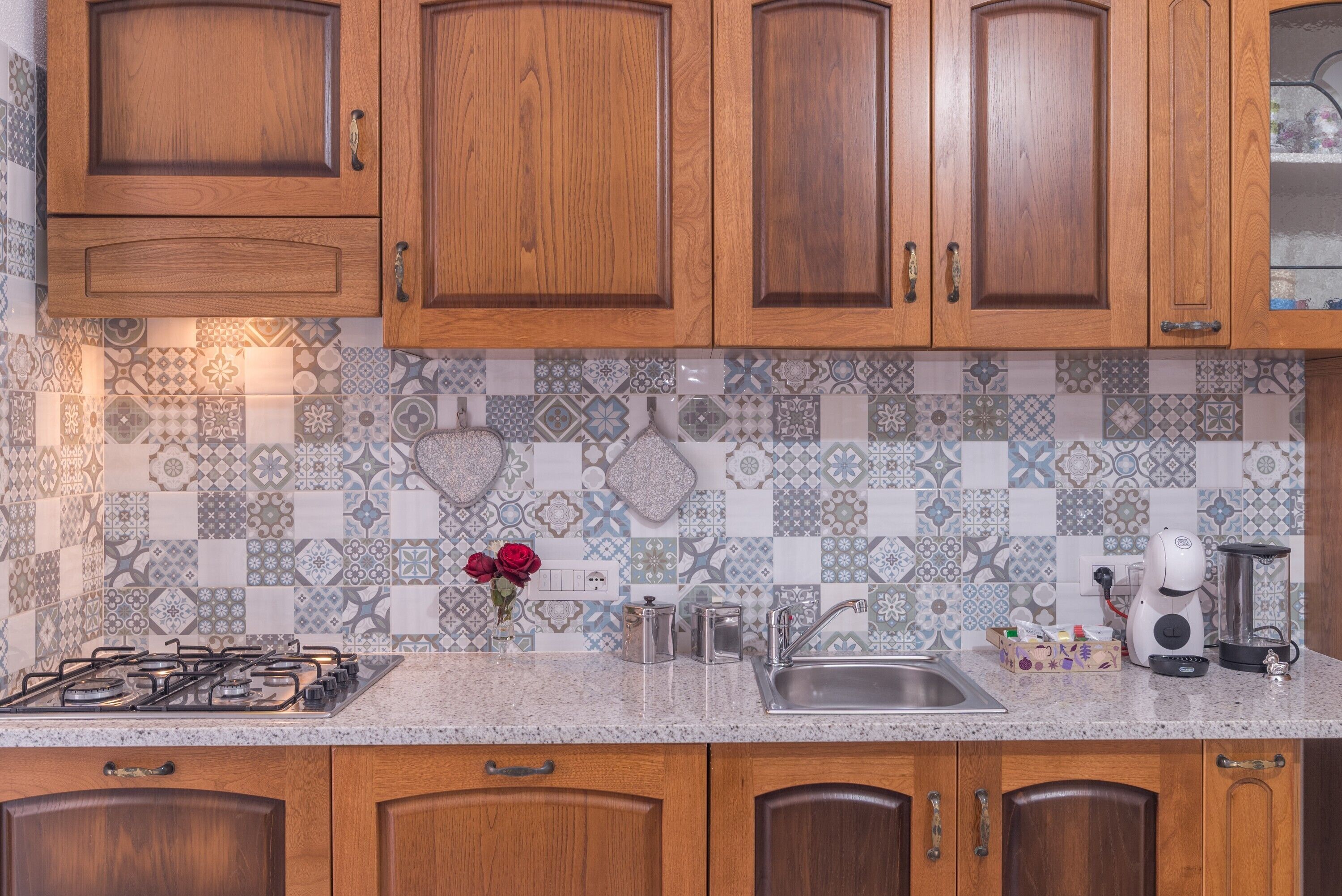A kitchen with wooden cabinets, a patterned backsplash, a gas stove, a sink, and a coffee maker.