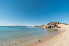 Une plage propre avec une eau calme, un rivage sablonneux et un promontoire rocheux.