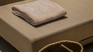 A sun lounger with a wooden side table holding a glass of white wine and a lemon slice. A folded towel is placed on the lounger. - Adrias Villa (Kefalonia)