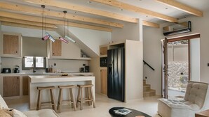 A modern kitchen with wooden beams, a central island with stools, a black refrigerator, and a dining area with a cushioned chair and a small table. - Adrias Villa (Kefalonia)
