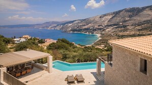 A view of a coastal property with a swimming pool, outdoor seating, and a scenic ocean and mountain backdrop. - Adrias Villa (Kefalonia)