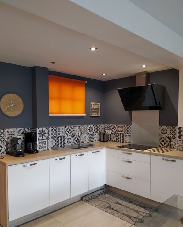 Modern kitchen with white cabinetry, black range hood, and oven, featuring a geometric tile backsplash and a window with a blind.