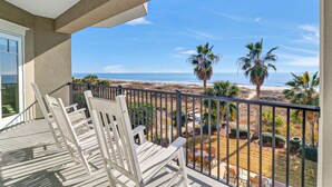 Ein Balkon mit weißen Stühlen mit Blick auf Strand und Palmen.