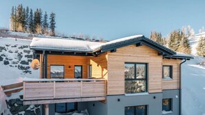 A modern wooden cabin with a balcony, large windows, and a stone foundation.