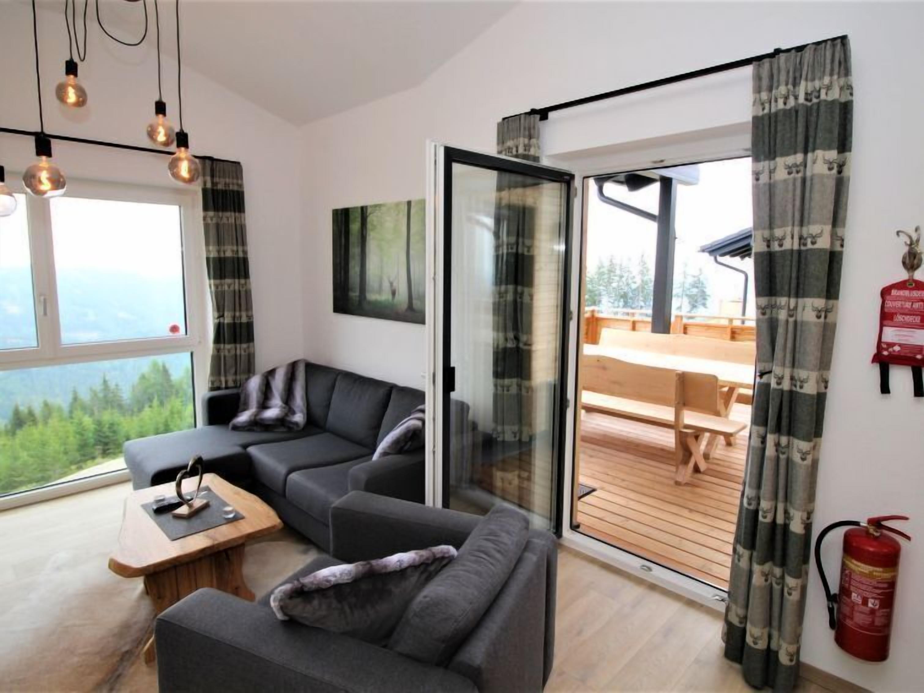 A modern living room with a sofa, a small table, and a glass door leading to an outdoor deck.