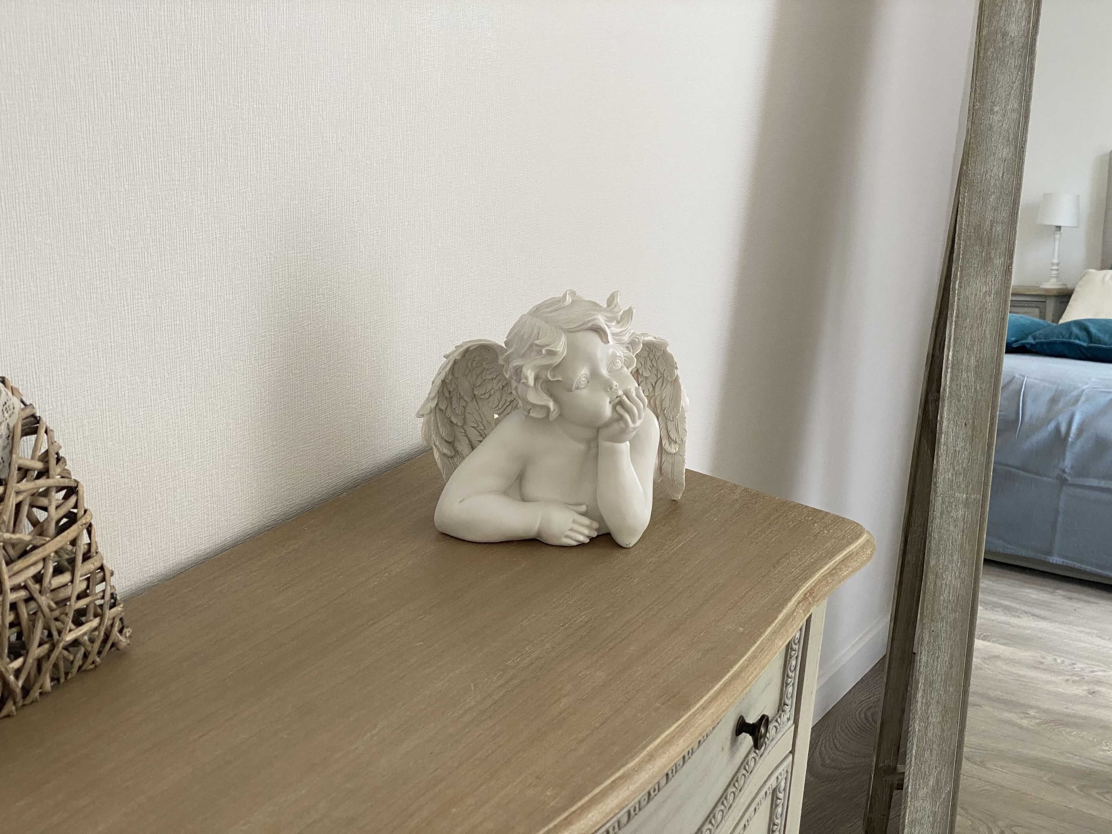 Une commode en bois sur laquelle est posée une statuette d’ange blanche.