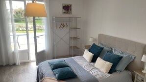 A bedroom with a bed, bedside tables, a hanging lamp, a window with curtains, and a view of greenery outside. - House with private pool and jacuzzi, panoramic river view (La Force)