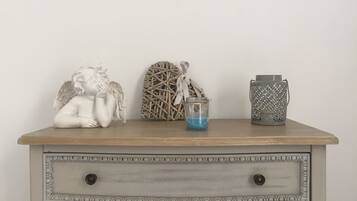 A wooden dresser with three decorative items: a white angel figurine, a woven basket with a blue candle, and a patterned metal container.