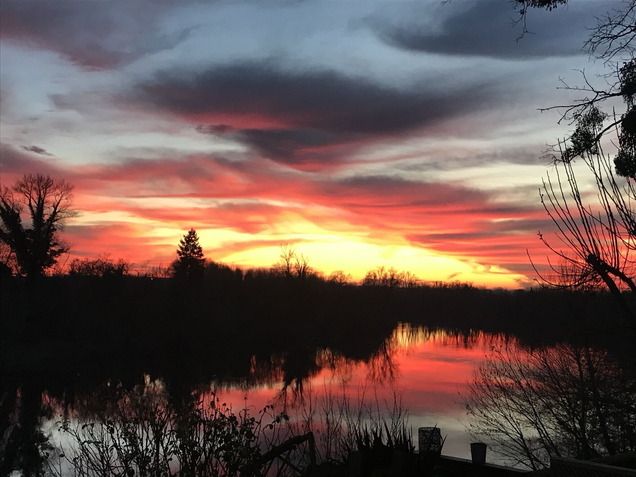 A sunset over a calm lake with silhouettes of trees and a dock.